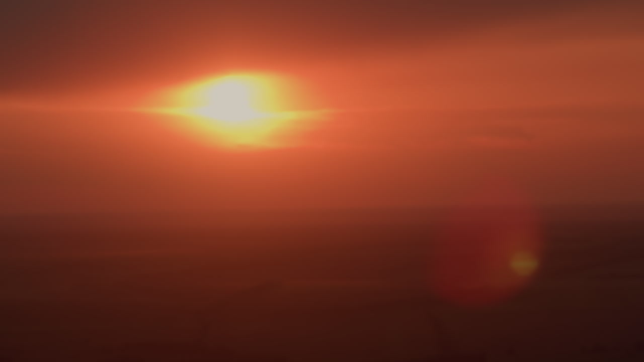 vibrant orange sunset over distant horizon with soft glowing sun casting warm hues across wispy clouds and fading day sky creating tranquil serene mood for nature backdrop evening