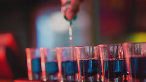 barman prepares party shots in nightclub closeup. barkeeper makes shooter sets pouring alcoholic drinks for party guests. hard drink for celebrations