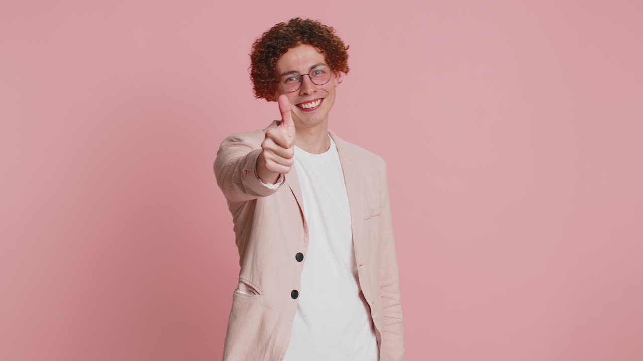 Young man with curly hair and glasses giving thumbs up