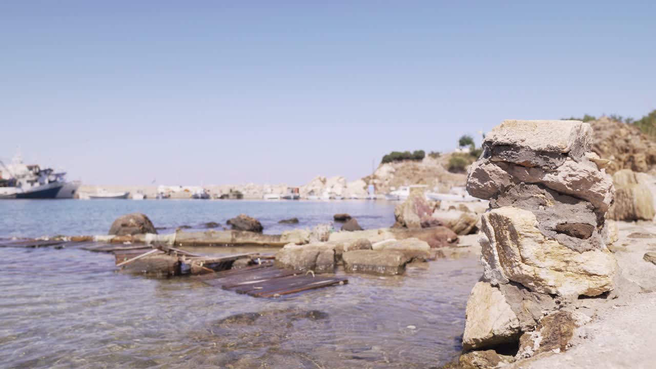 Serene coastal scene with clear blue water, old ruins and broken wooden planks on shore.