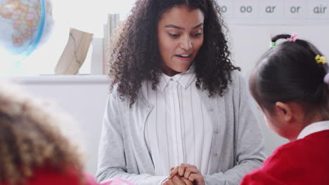 female kindergarten teacher sitting at a table in class talking to a chinese schoolgirl, close up