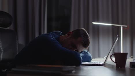 empresario cansado durmiendo frente a la computadora portátil debido al exceso de trabajo nocturno en el lugar de trabajo oscuro de la oficina en casa