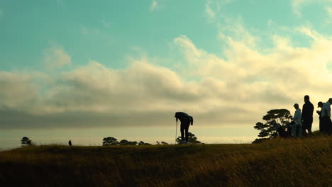 Group-of-golfers-silhouetted-against-dramatic-sky-with-moving-clouds,-evening,-zooming-in