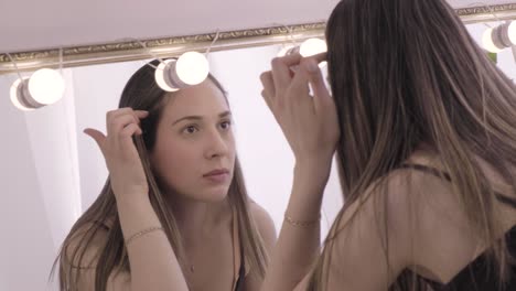 model examining her face by looking into a lighted makeup mirror in the studio