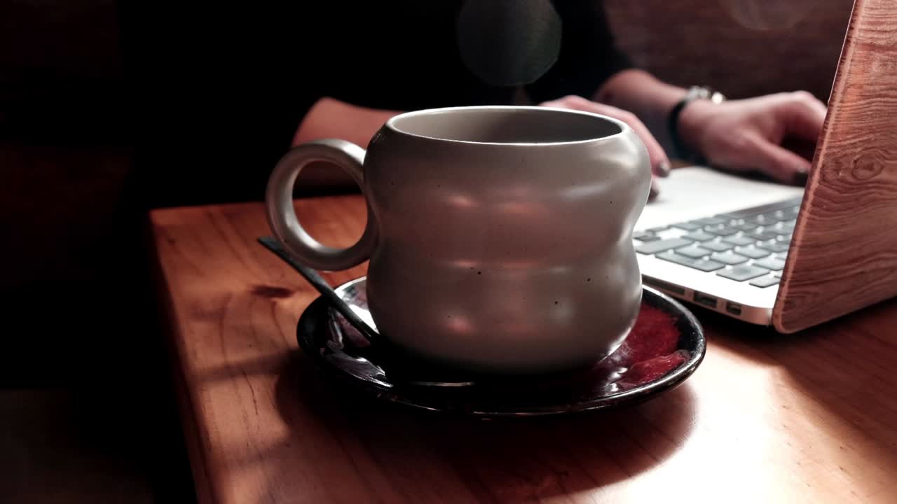 mujer trabajando en su computadora portátil en un café con una bebida caliente
