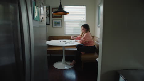 stressed out woman writing at kitchen table in the afternoon by the window, barefoot in pink sweater