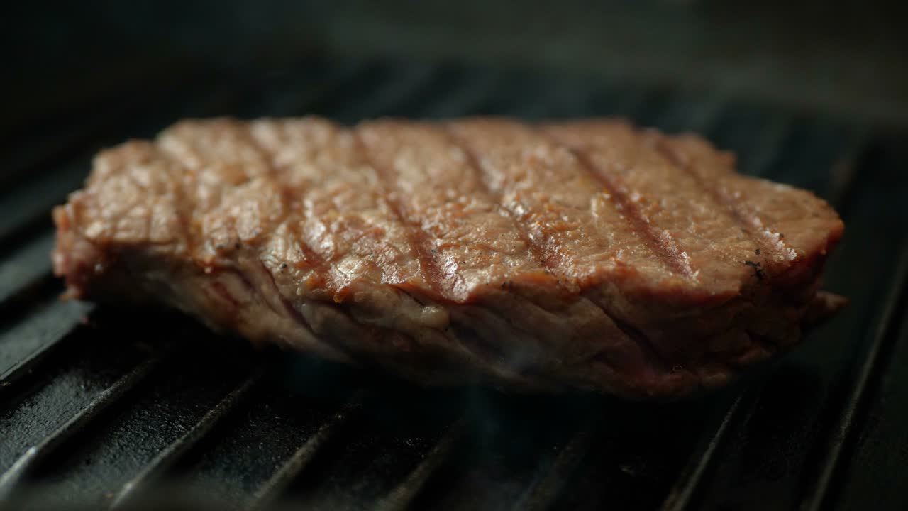 Fresh beef meat on ignited pan closeup view. Cinemagraph of cooking beef steak at frying pan, steak fried on a grill pan.