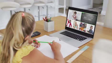 Schoolgirl-using-laptop-for-online-lesson-at-home,-with-diverse-teacher-and-class-on-screen