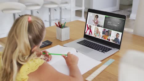 schoolgirl using laptop for online lesson at home, with diverse teacher and class on screen