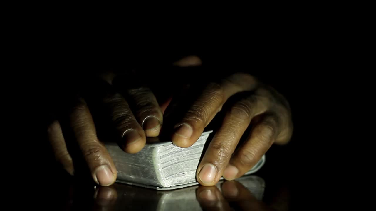 hombre rezando a dios con las manos juntas sobre fondo negro con la gente almacen de video