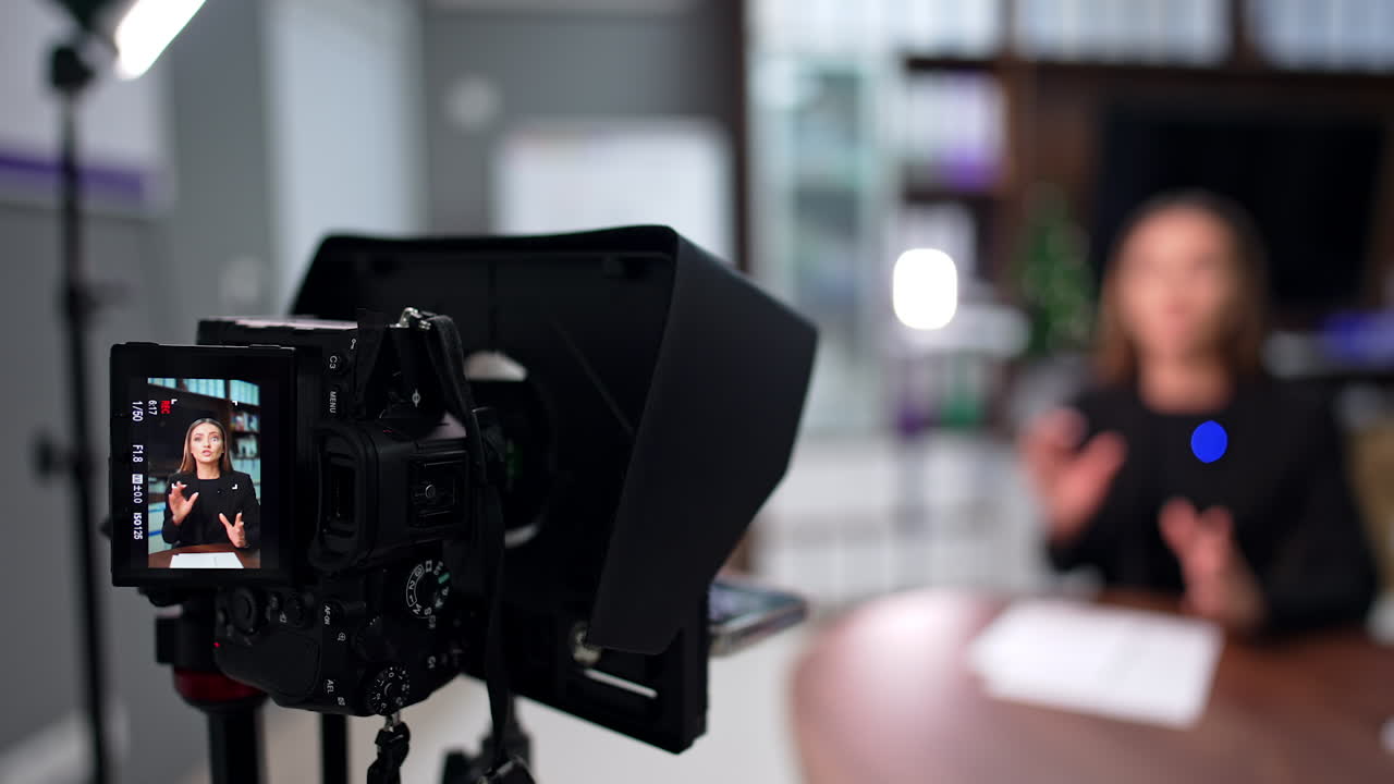 Woman sitting in the office talks to camera gesturing. Female blogger recording a content for her blog. Blurred backdrop.