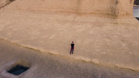 attractive young man standing next to a coastal cliff at sunset - aerial drone shot