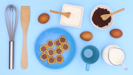 flour, milk, eggs and cookies tools appear with sweet cookies in blue plate on blue theme. stop motion