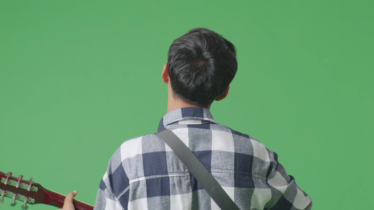 녹색 스크린 배경에서 기타를 연주하고 노래하는 젊은 아시아 십대 소년의 가까운 뒷면