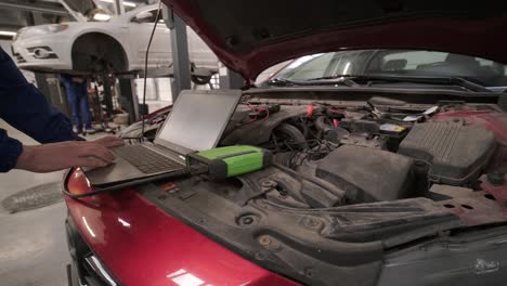 computer diagnostics of cars, young mechanic specialist male uses laptop technology while repairing vehicle with open hood at service station