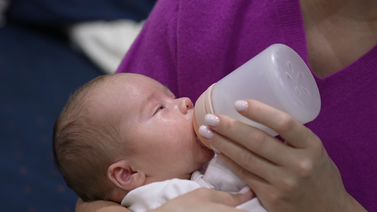Newborn baby boy having meal and slowly falling asleep. Tiny boy in mother's hands going to sleep while feeding. Adorable kid close up.