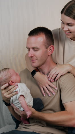 new-made dad looks at his newborn son with adoration holding him in hands. mom sits behind her husband.. vertical video