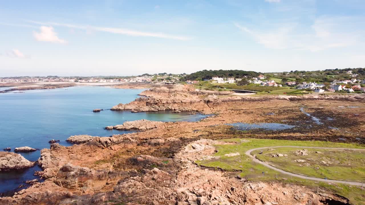 Costa di Guernsey sorvolando promontori, baie, rocce e mare azzurro limpido con spiagge, campi e case in lontananza in una luminosa giornata di sole