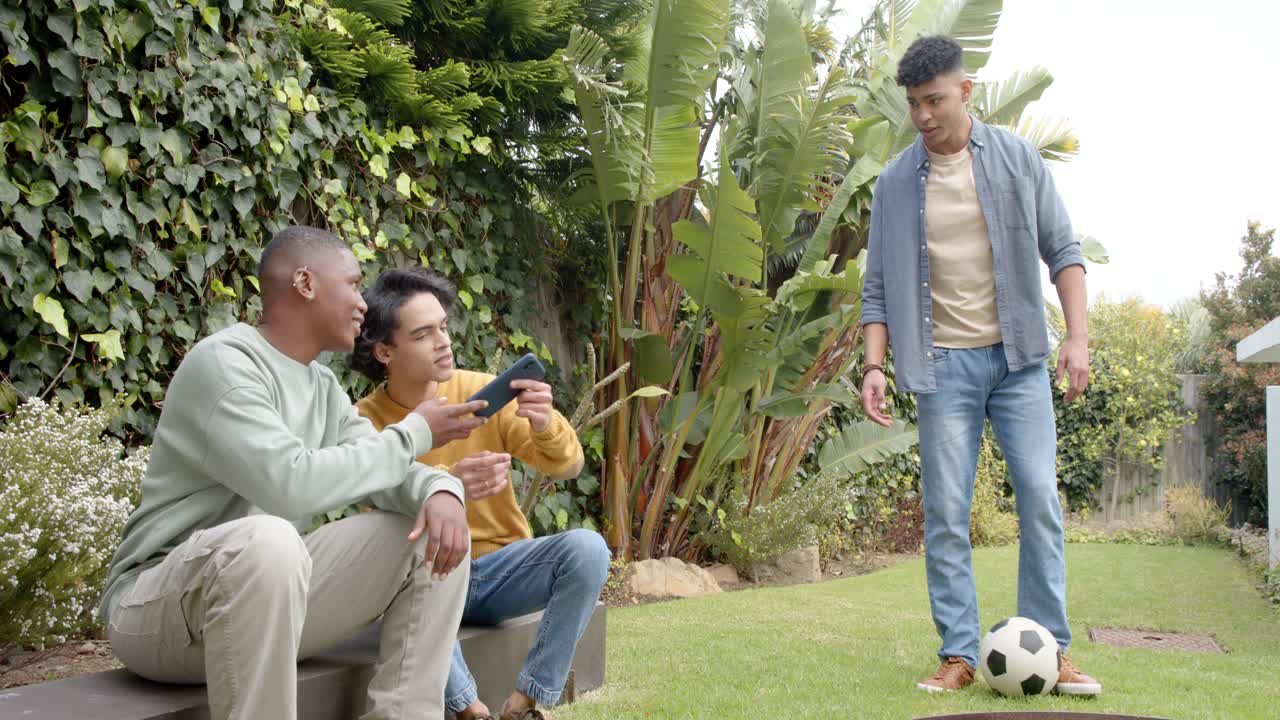 Smartphone prompt inspiring diverse friends pointing and urging friend dribbling ball in garden