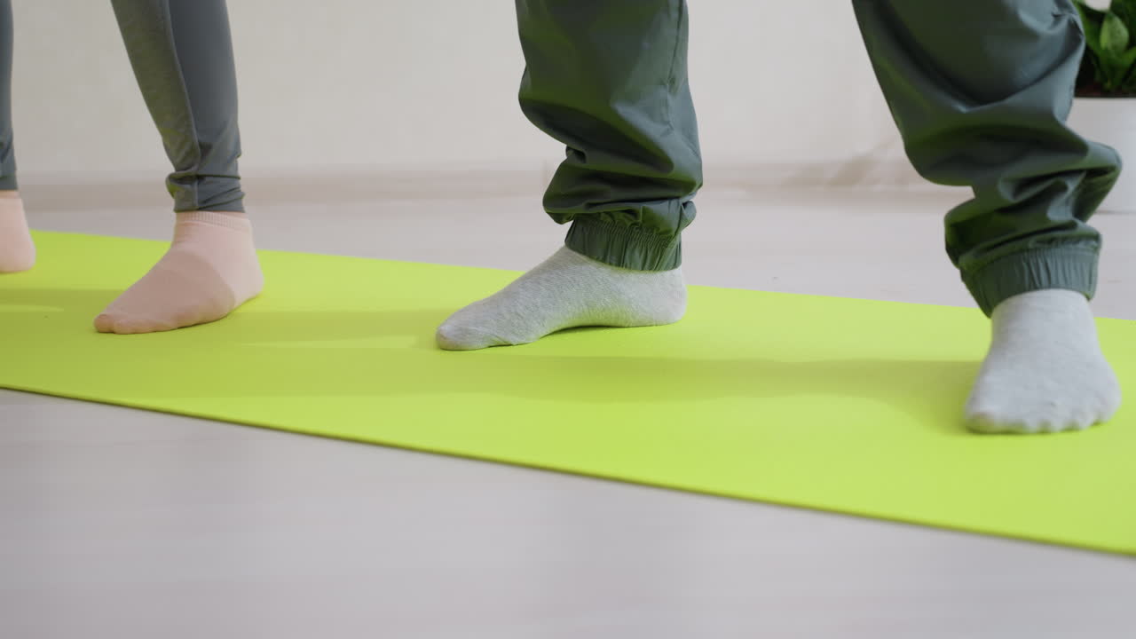 Leg view of people exercising on bright green fitness mat indoors, showing socks and lower body movement, capturing workout and training