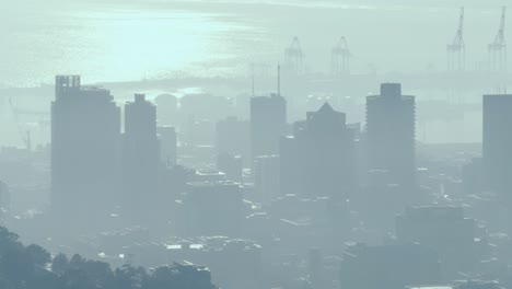 general view of cityscape with multiple modern buildings and shipyard covered in smog