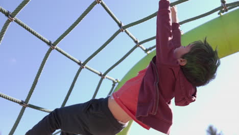 young boy climbs upside down on playstructure on sunny spring day