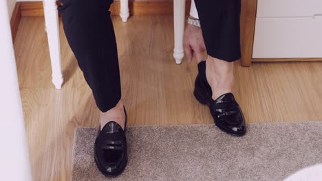 man in formal pants stepping into polished black dress shoes indoors