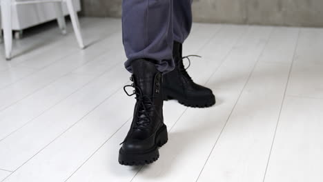 black massive army boots with laces on model's legs. woman walks in stylish footwear on the white floor in studio. top view close up.