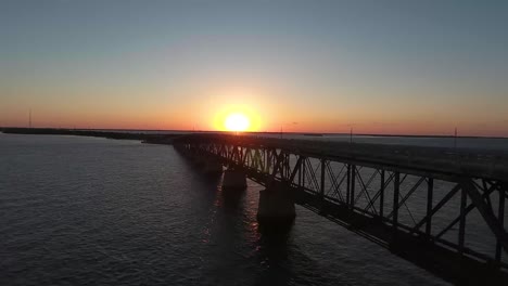 AERIAL:-Pull-back-and-rise-up-over-an-old-bridge-in-the-middle-of-the-ocean-at-sunset