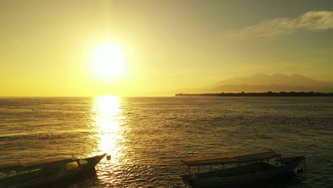 yellow sun setting down the horizon coloring golden sky, reflecting over tranquil sea surface where are anchored fishing boats in bali