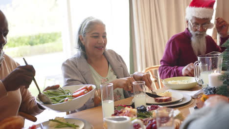 Felices-Y-Diversos-Amigos-Mayores,-Hombres-Y-Mujeres,-Sirviendo-Cena-De-Navidad-En-La-Mesa,-Cámara-Lenta