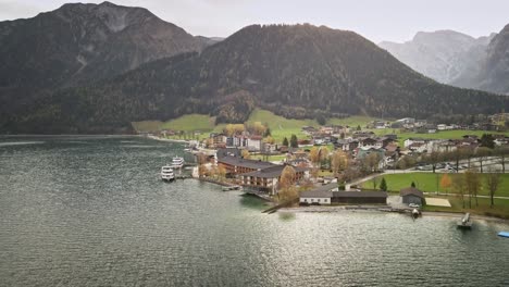 a captivating drone shot from achensee pertisau, flying outward to reveal the picturesque lake town surrounded by mountains and vibrant turquoise waters. a serene alpine scene in austria.