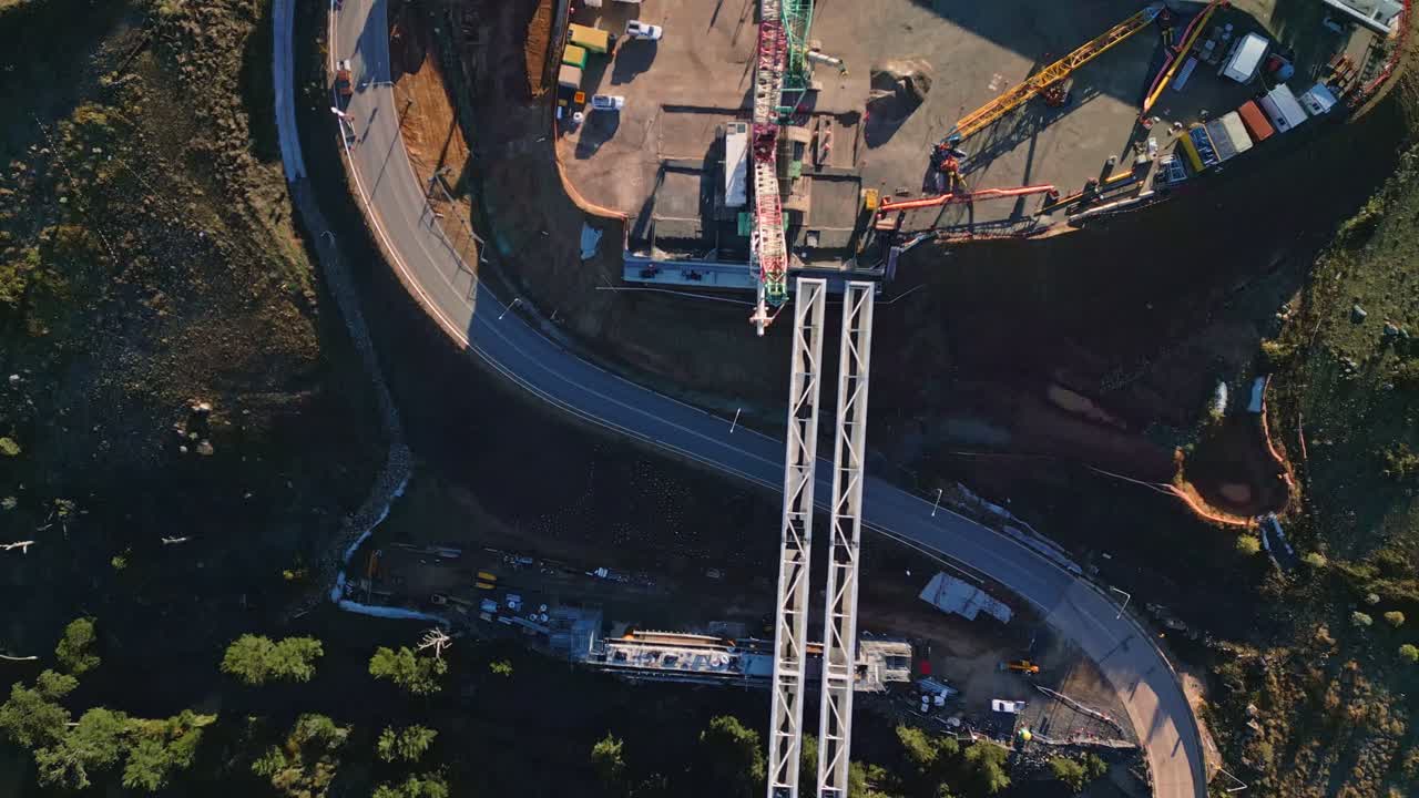 Aerial footage directly above the Molonglo Bridge construction site in Canberra, showcasing cranes lifting large steel beams into place over the river.