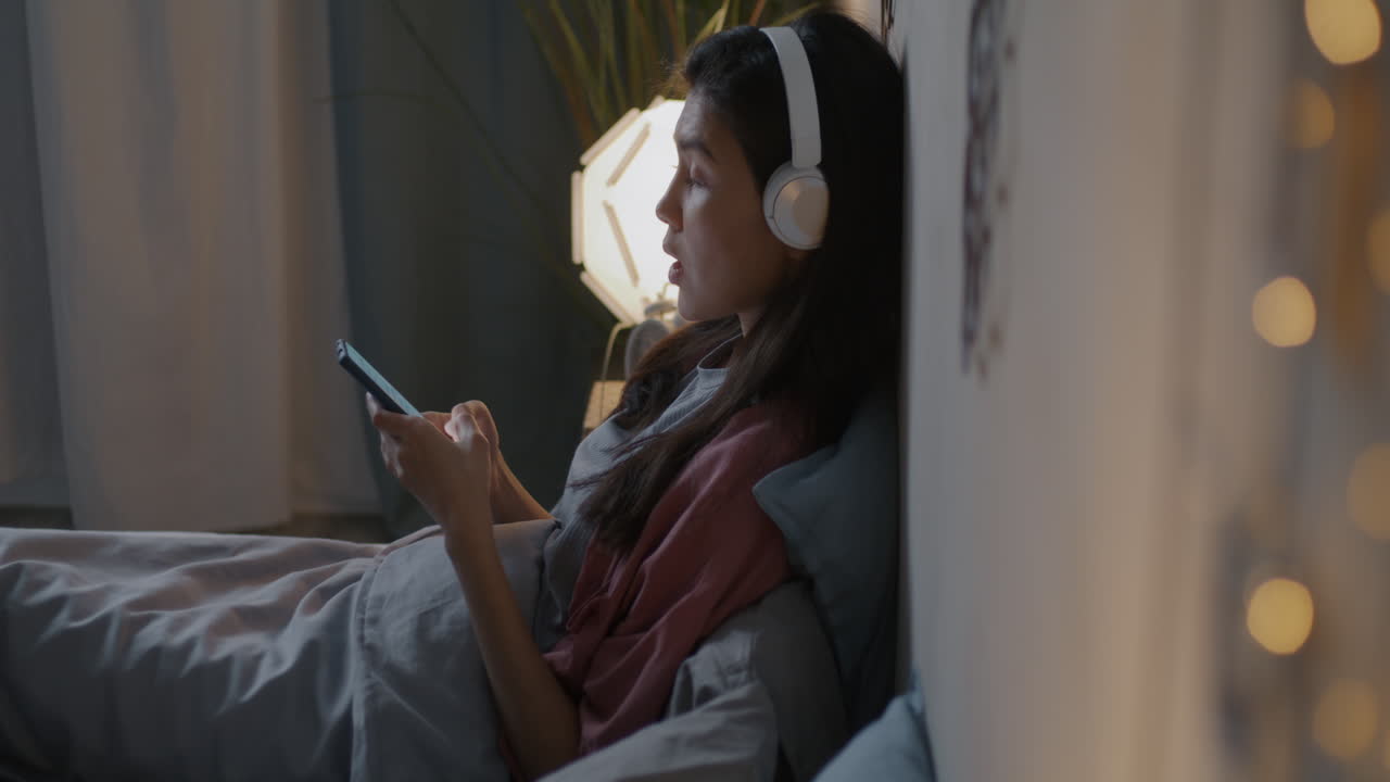 헤드폰과 전화로 침대에서 휴식을 취하는 여자