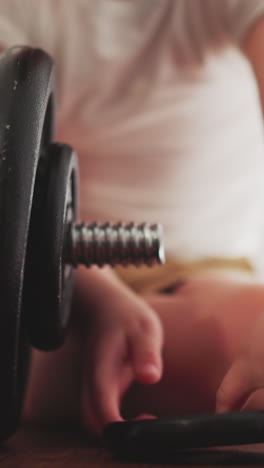 little boy puts black rings on heavy barbell for workout sitting on floor. toddler prepares gym equipment for intensive training closeup slow motion