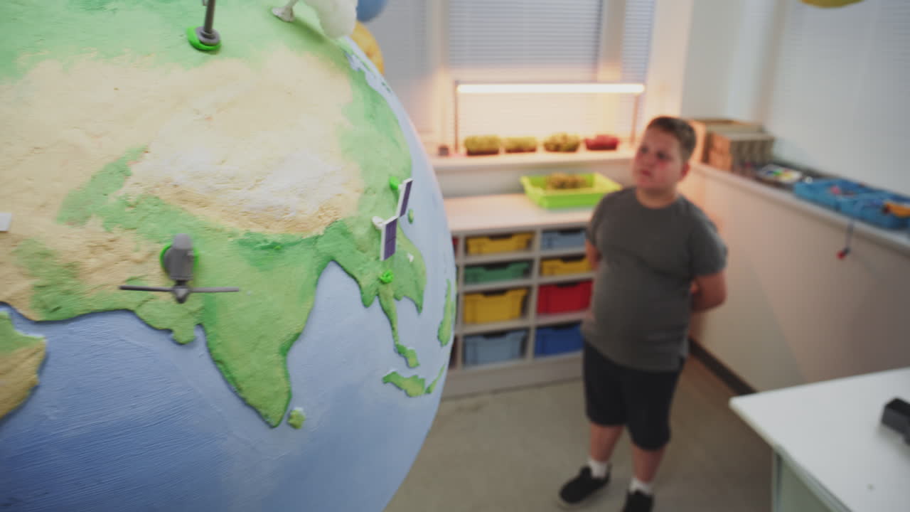 Elementary School Student Looking at Miniature Models of Wind Turbines and Solar Panels on Globe