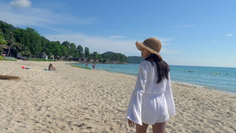 Woman-in-a-white-sundress-and-brown-hat-strolls-on-a-beautiful-sandy-beach