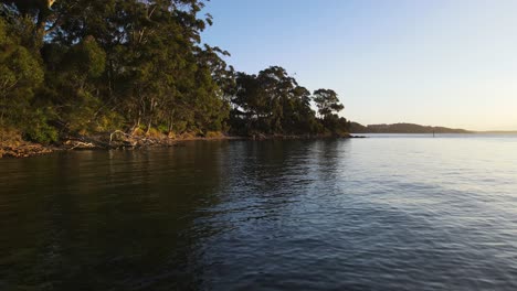 Revealing-drone-view-travelling-over-calm-water-next-to-a-rugged-coastline-covered-in-native-bushland