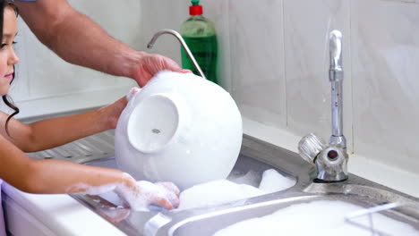 a father is teaching his daughter to wash the dishes