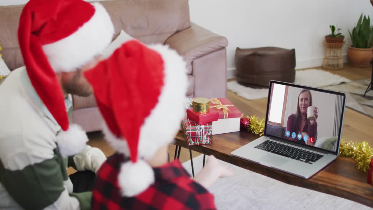 padre y hijo caucásicos usando sombreros de santa en una videochat portátil durante la navidad en casa