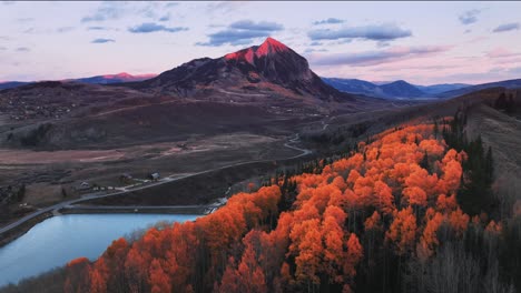 a drone view of water, golden and orange aspens, and the tip of a mountain in crested butte, co being lit up by alpen glow