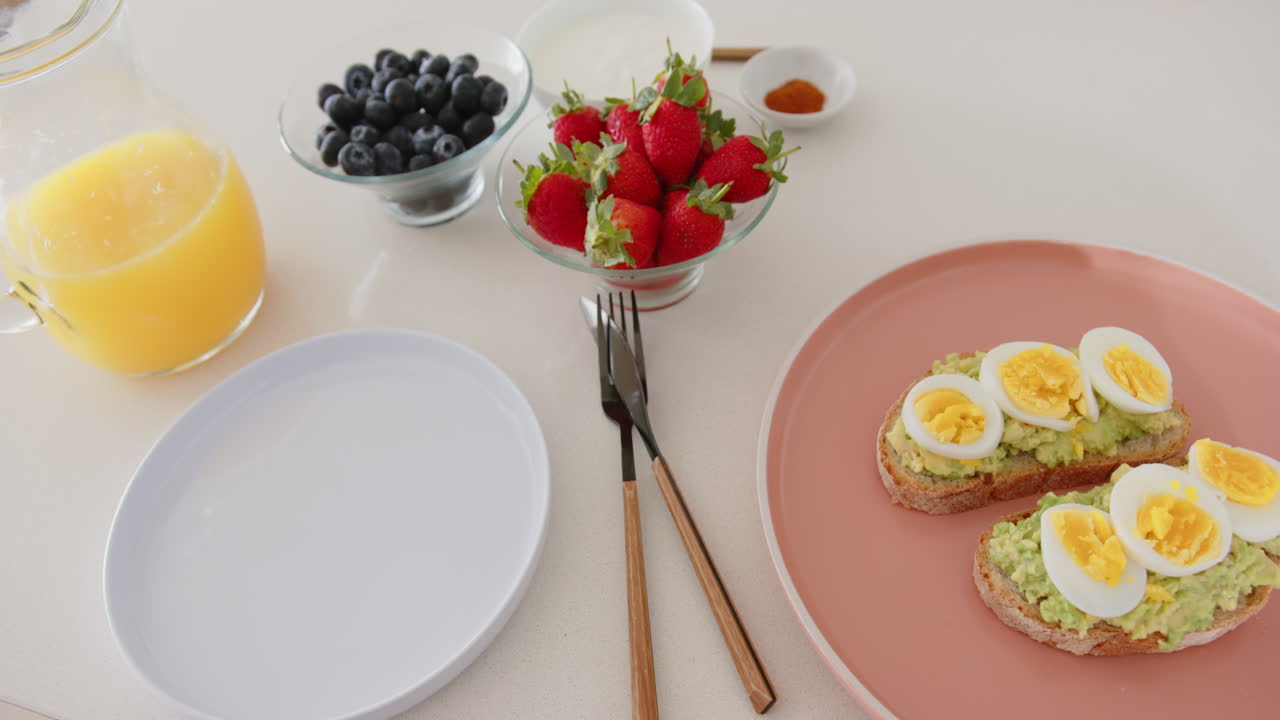 Eating healthy breakfast with avocado toast, boiled eggs, berries, and orange juice, at home