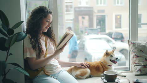 woman reading a book with her dog by the window