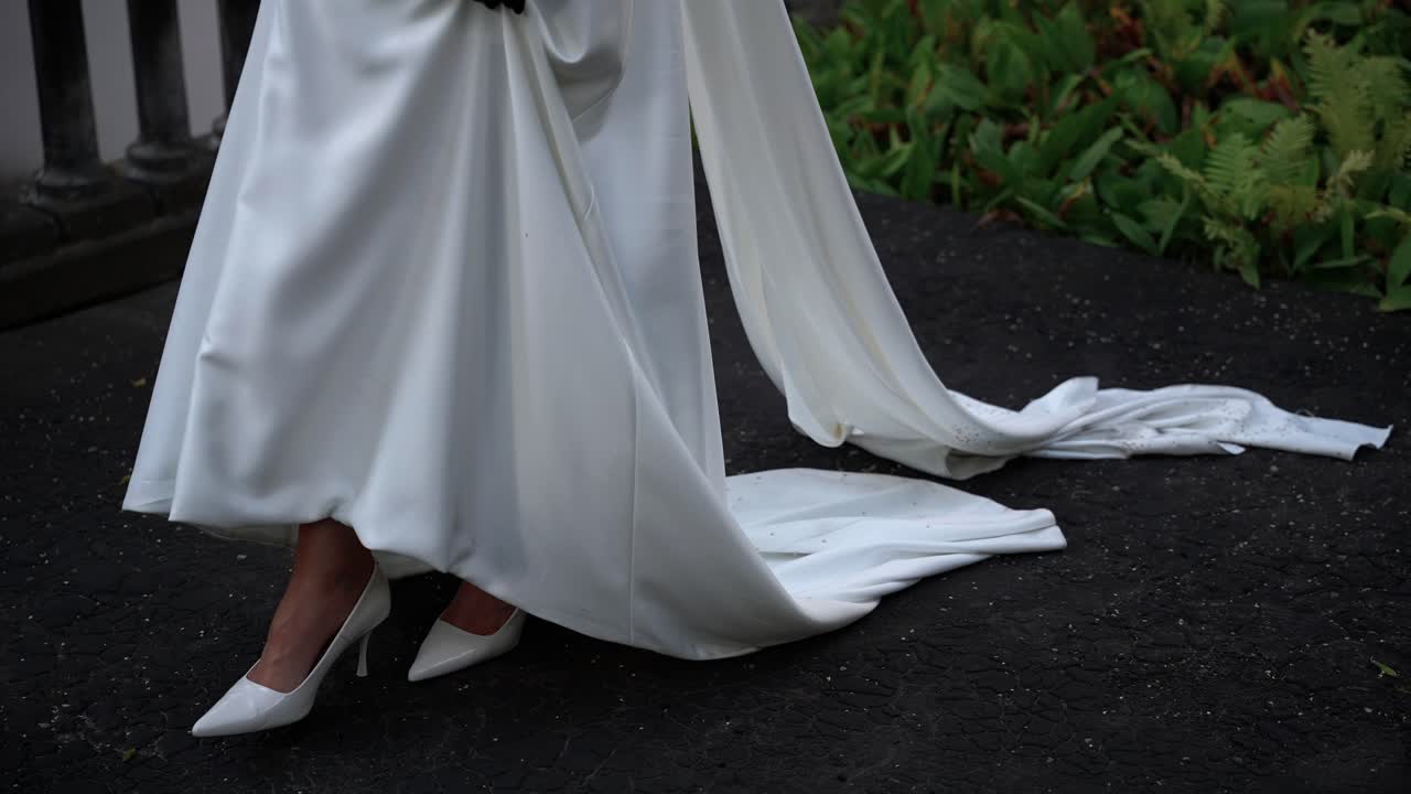 Close-up of a bride walking outdoors in an elegant white wedding gown with high heels, capturing the flowing train and graceful movement during a romantic and stylish wedding moment