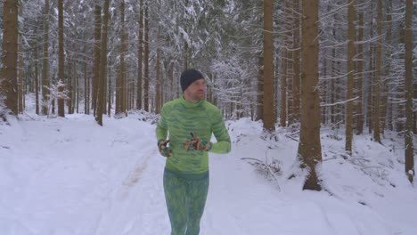 hombre atlético con traje verde corriendo en el bosque en un sendero nevado durante el frío día de invierno - siga el tiro, cámara lenta