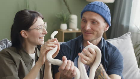 vista posteriore di una donna che tiene un serpente e parla con il suo ragazzo che tiene anche un serpente