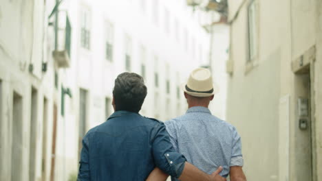 back view of happy guy couple walking down lane and hugging