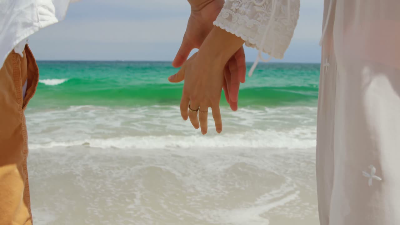 sección media de una pareja caminando de la mano en la playa 4k