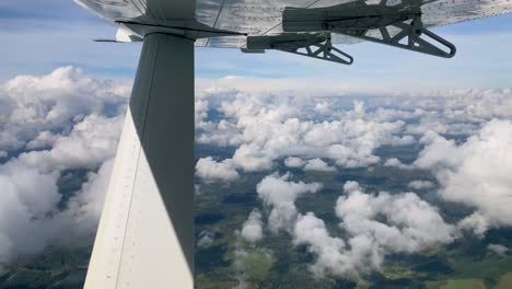 view from small airplane flying over puffy white clouds and green landscape