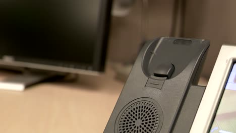 un primer plano de una mano levantando y golpeando un teléfono de oficina contra la base del teléfono en un cubículo de oficina